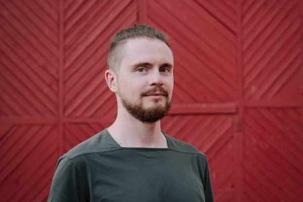 Pavel in front of a red wooden gate, wearing a dark green t-shirt, slightly smiling